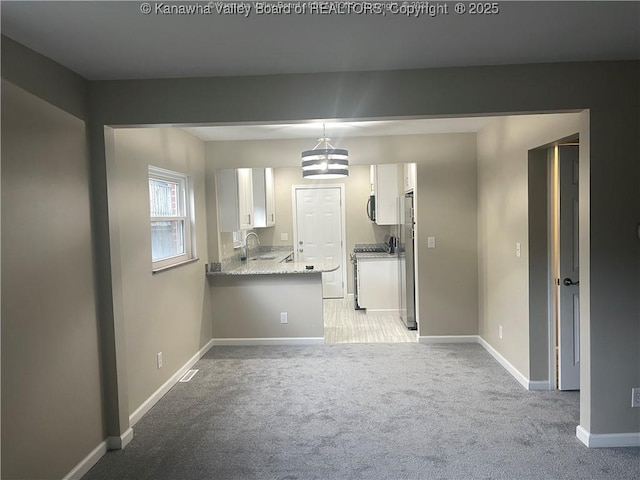 kitchen featuring stainless steel appliances, light colored carpet, white cabinets, a sink, and a peninsula