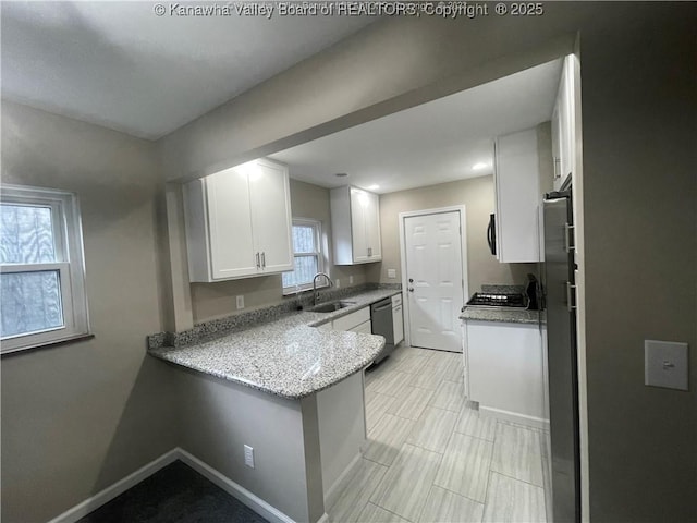 kitchen featuring appliances with stainless steel finishes, white cabinetry, a sink, a peninsula, and baseboards