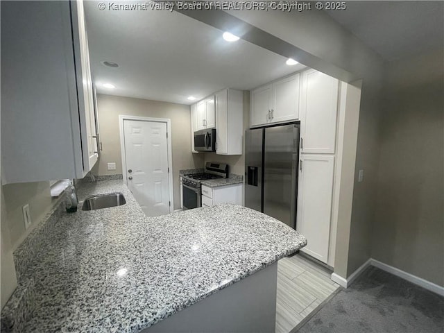 kitchen featuring baseboards, white cabinets, appliances with stainless steel finishes, light stone counters, and a peninsula