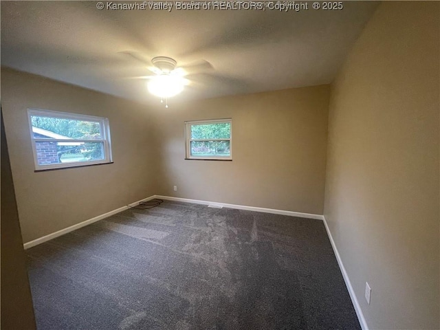 spare room with a ceiling fan, baseboards, dark colored carpet, and a wealth of natural light