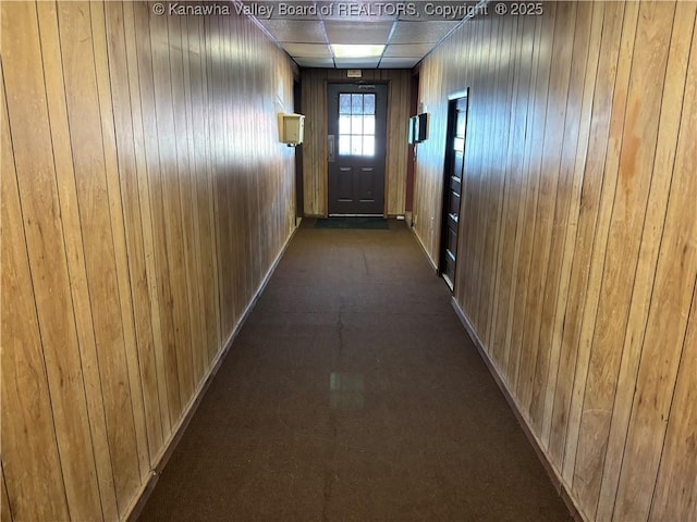 corridor featuring wood walls, a paneled ceiling, and baseboards