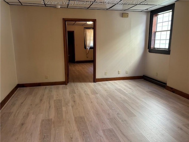 empty room featuring a baseboard heating unit, light wood-type flooring, a paneled ceiling, and baseboards