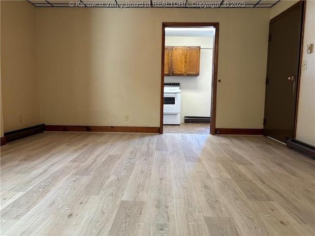 empty room with a baseboard heating unit, light wood finished floors, and baseboards