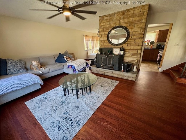 living room with a textured ceiling, a wood stove, dark wood-style floors, and a ceiling fan