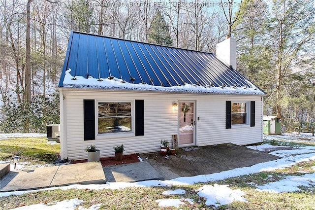 view of front of house with a patio, a chimney, metal roof, a standing seam roof, and central air condition unit