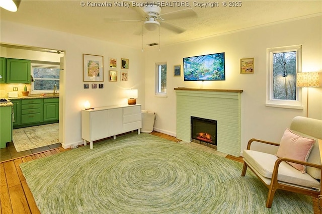 sitting room featuring a brick fireplace, ceiling fan, baseboards, and wood finished floors