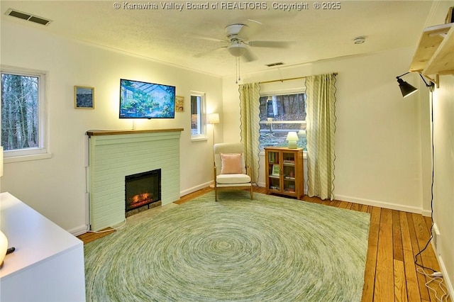 sitting room featuring a healthy amount of sunlight, a brick fireplace, visible vents, and wood finished floors