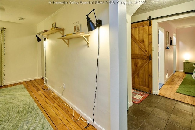 hall with baseboards, a barn door, ornamental molding, and wood finished floors