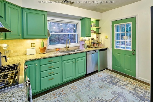 kitchen featuring decorative backsplash, stainless steel appliances, wall chimney range hood, green cabinets, and a sink