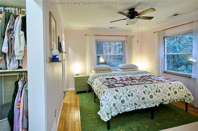 bedroom with light wood-type flooring, multiple windows, visible vents, and ornamental molding