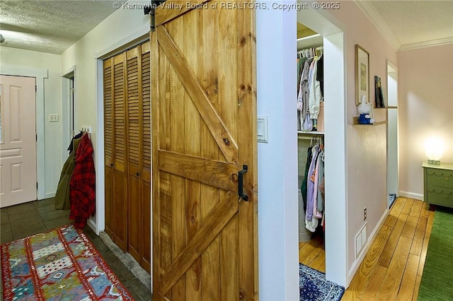 hallway featuring visible vents, a barn door, ornamental molding, a textured ceiling, and wood finished floors