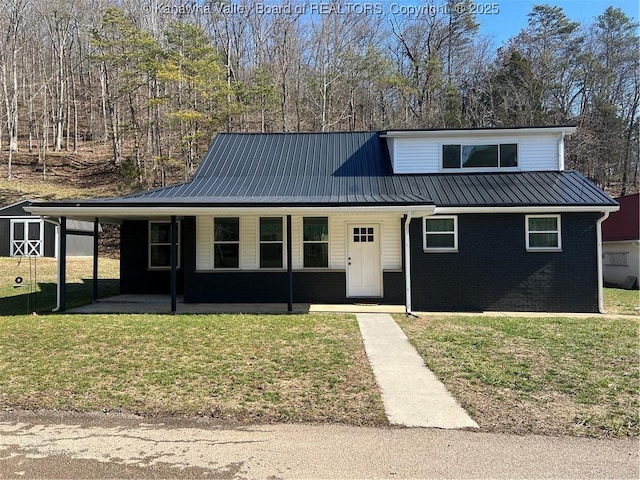 view of front of property with metal roof, an outbuilding, covered porch, a front lawn, and brick siding