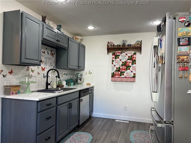 kitchen featuring baseboards, decorative backsplash, dark wood-style flooring, stainless steel appliances, and a sink