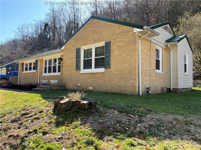 view of side of property featuring crawl space, brick siding, and a lawn