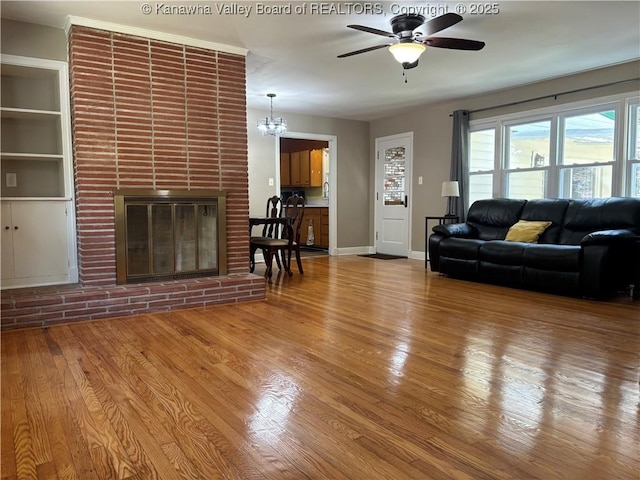 unfurnished living room with ceiling fan with notable chandelier, a fireplace, baseboards, and wood finished floors