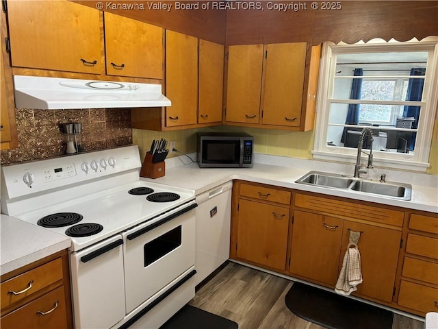 kitchen with white appliances, under cabinet range hood, light countertops, and a sink