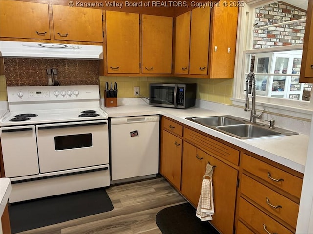 kitchen featuring under cabinet range hood, white appliances, a sink, light countertops, and light wood-type flooring