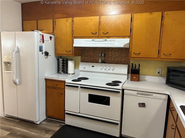 kitchen featuring under cabinet range hood, white appliances, wood finished floors, light countertops, and decorative backsplash