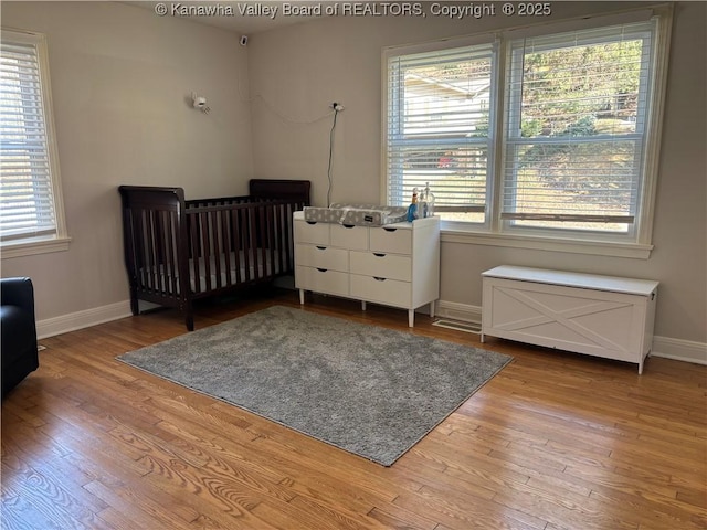 bedroom featuring light wood-type flooring, baseboards, and a crib