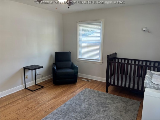 bedroom featuring a nursery area, baseboards, visible vents, and wood finished floors