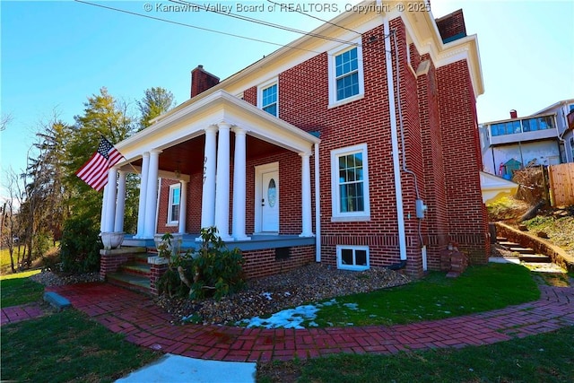 view of front of property with covered porch, a chimney, and brick siding