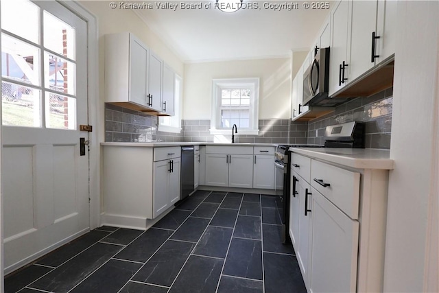 kitchen with white cabinets, appliances with stainless steel finishes, a sink, light countertops, and backsplash