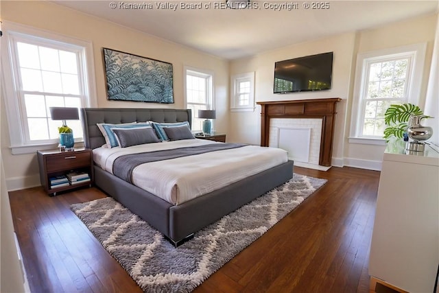 bedroom featuring a tiled fireplace, baseboards, and dark wood-type flooring