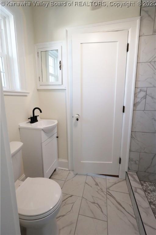 bathroom with toilet, marble finish floor, tiled shower, and vanity