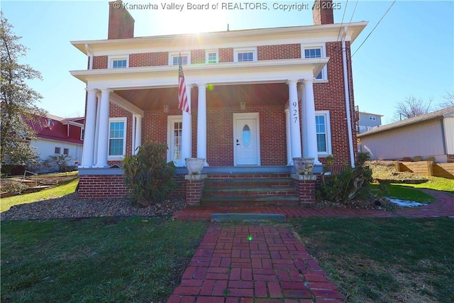 view of front facade with a front yard, covered porch, a chimney, and brick siding