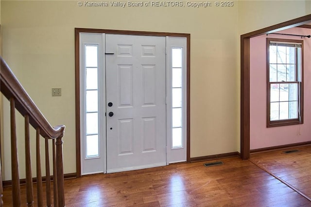 entryway with stairway, wood-type flooring, visible vents, and baseboards