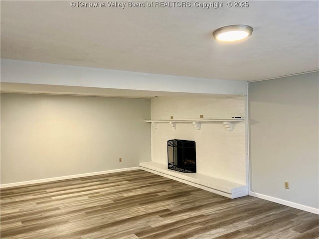 unfurnished living room featuring a fireplace with raised hearth, wood finished floors, and baseboards