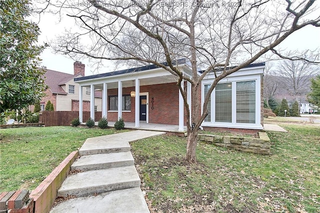 view of front of home featuring a porch, brick siding, fence, and a front lawn