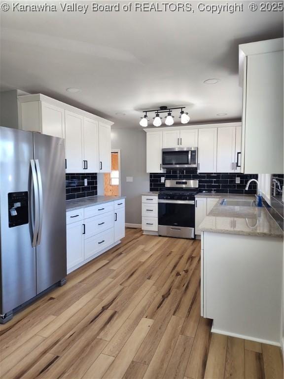 kitchen featuring light wood finished floors, appliances with stainless steel finishes, white cabinets, and a sink