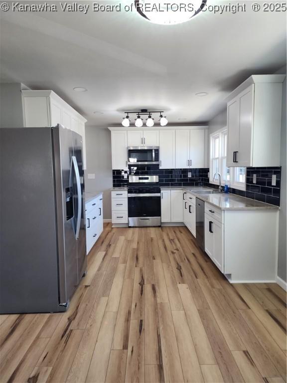 kitchen featuring light wood-type flooring, a sink, stainless steel appliances, and decorative backsplash