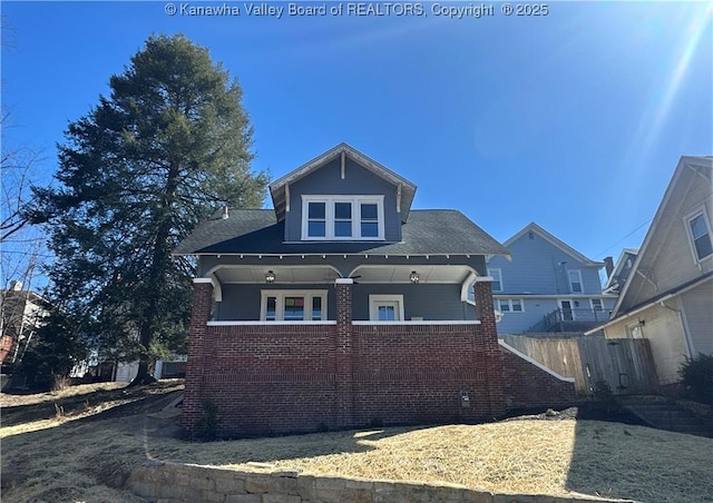 rear view of house with fence, a porch, and brick siding