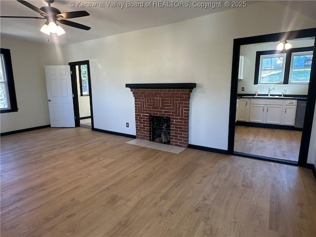 unfurnished living room featuring plenty of natural light, light wood-type flooring, a fireplace, and a sink