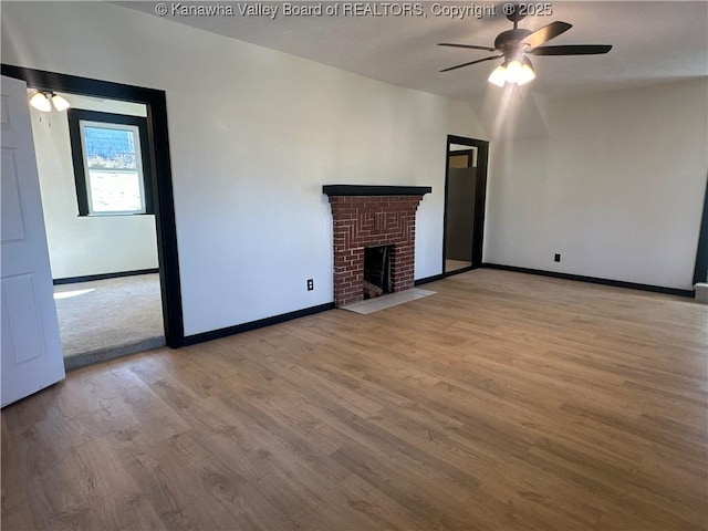 unfurnished living room featuring a brick fireplace, ceiling fan, baseboards, and wood finished floors