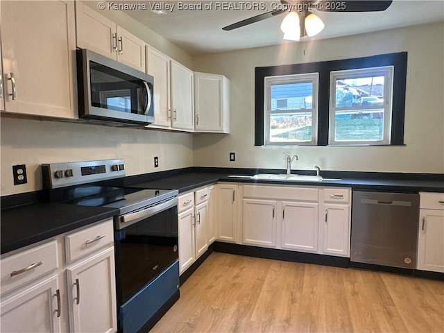 kitchen featuring stainless steel appliances, a sink, white cabinets, light wood finished floors, and dark countertops