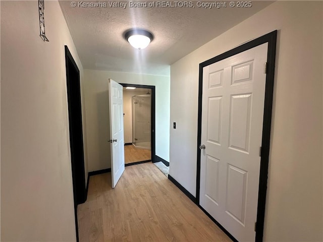 hallway with baseboards, a textured ceiling, and light wood finished floors