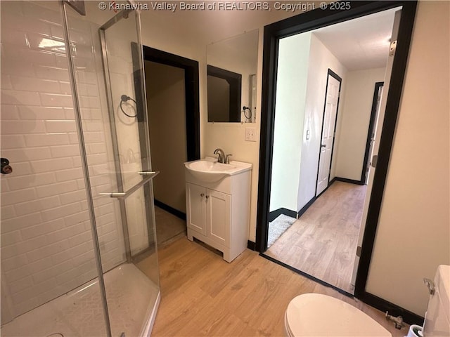 bathroom featuring toilet, a stall shower, vanity, wood finished floors, and baseboards