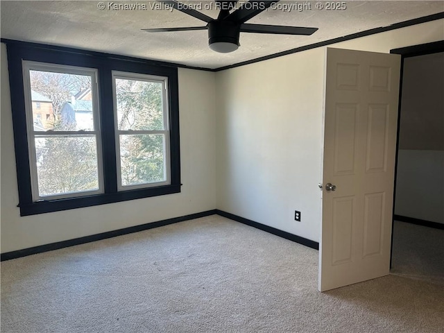 carpeted spare room with a textured ceiling, ornamental molding, a ceiling fan, and baseboards