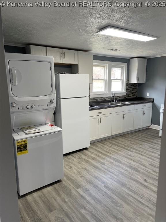 kitchen featuring a textured ceiling, stacked washer and dryer, a sink, freestanding refrigerator, and light wood finished floors