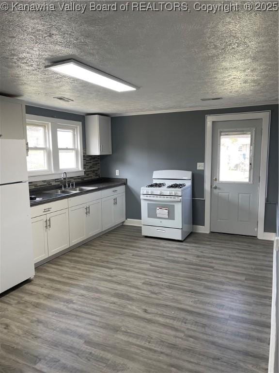 kitchen featuring dark wood-type flooring, dark countertops, white appliances, and a sink