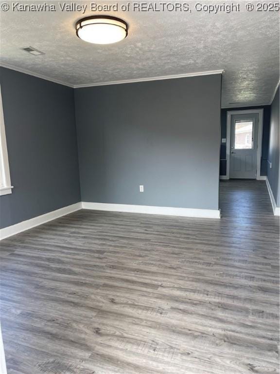 empty room featuring a textured ceiling, wood finished floors, visible vents, baseboards, and crown molding