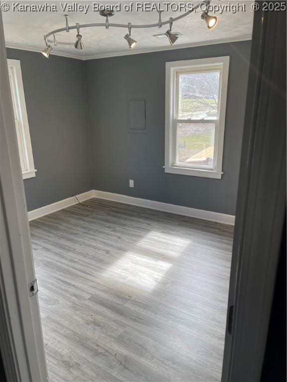 spare room featuring rail lighting, baseboards, crown molding, and wood finished floors