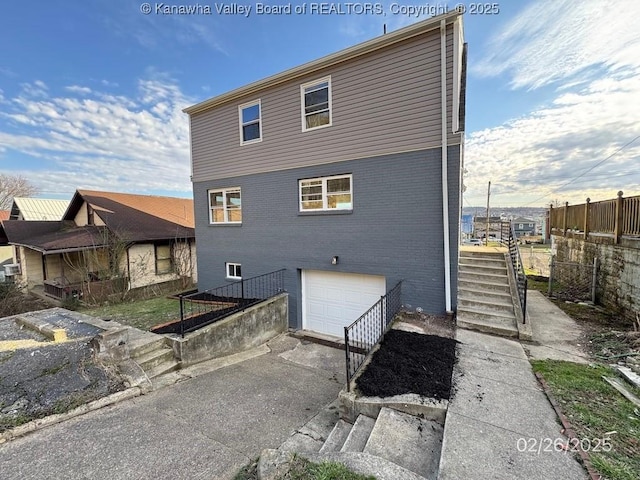 rear view of property featuring a garage, driveway, fence, and brick siding