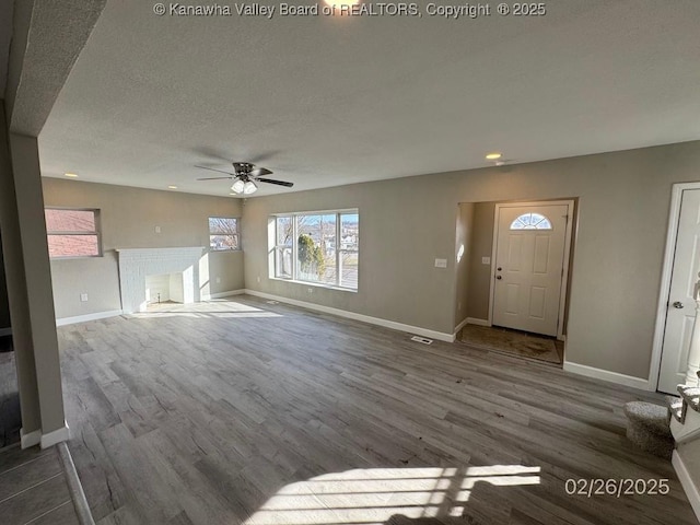 unfurnished living room featuring ceiling fan, a fireplace, wood finished floors, and baseboards