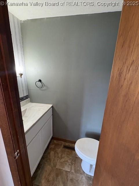 half bathroom featuring baseboards, vanity, and toilet