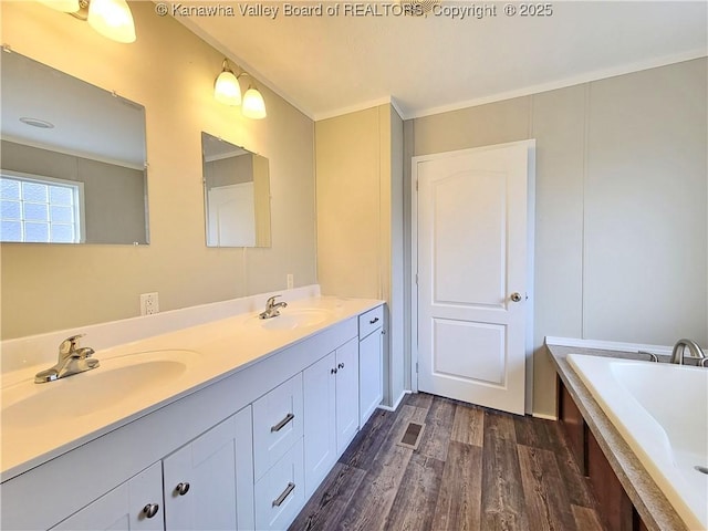 full bath with double vanity, a bathtub, a sink, and wood finished floors