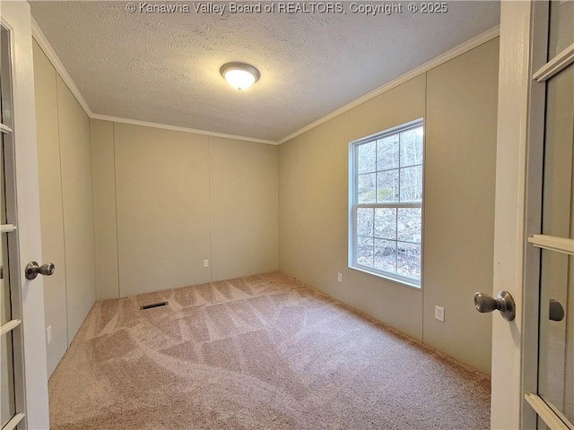 carpeted spare room with visible vents, ornamental molding, and a textured ceiling